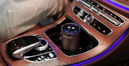 A sleek, portable EV air purifier with a real-time air quality display sitting in the center console of a Tesla