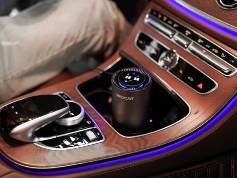 A sleek, portable EV air purifier with a real-time air quality display sitting in the center console of a Tesla