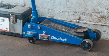 A technician using a black rubber EV jack pad to safely lift an electric vehicle in a professional garage
