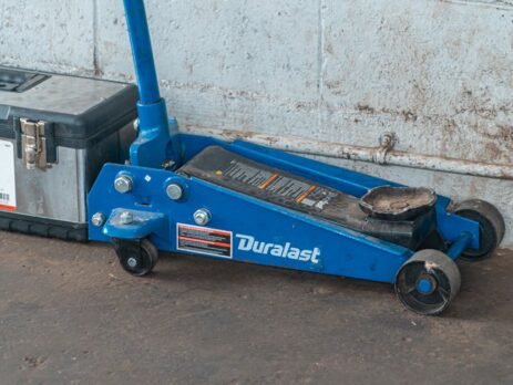 A technician using a black rubber EV jack pad to safely lift an electric vehicle in a professional garage