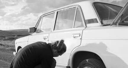 A portable EV tire repair kit with a 12V compressor and sealant bottle placed next to a Tesla Model 3 tire on the roadside