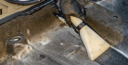 A person using a compact, high-power portable vacuum cleaner to clean the crevices of a Tesla Model 3 vegan leather seat