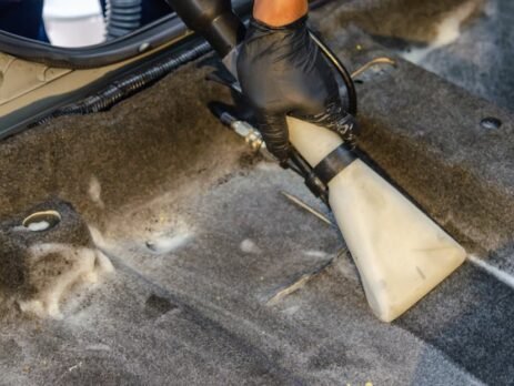 A person using a compact, high-power portable vacuum cleaner to clean the crevices of a Tesla Model 3 vegan leather seat