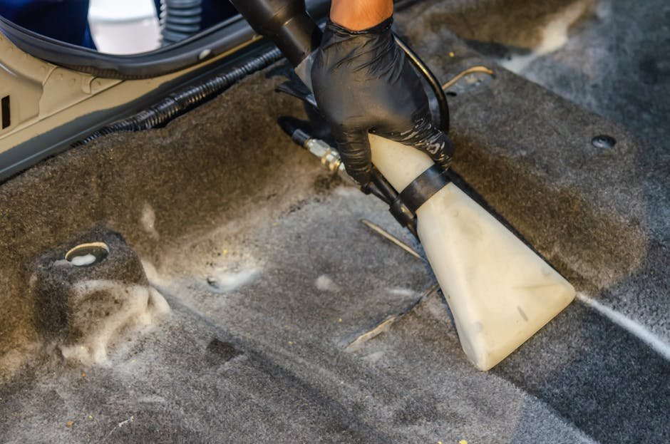 A person using a compact, high-power portable vacuum cleaner to clean the crevices of a Tesla Model 3 vegan leather seat